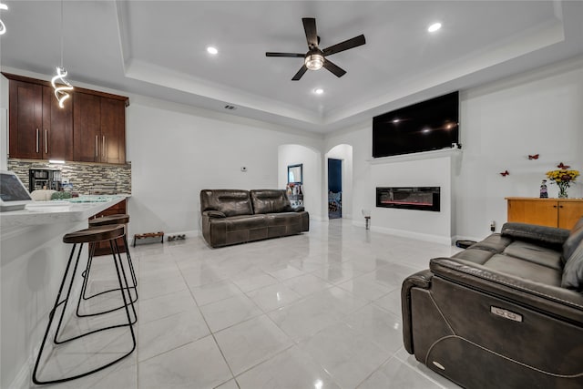 tiled living room featuring crown molding, a tray ceiling, and ceiling fan