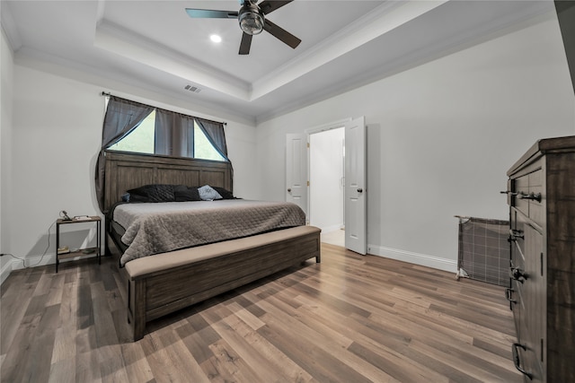 bedroom with ornamental molding, hardwood / wood-style flooring, a tray ceiling, and ceiling fan