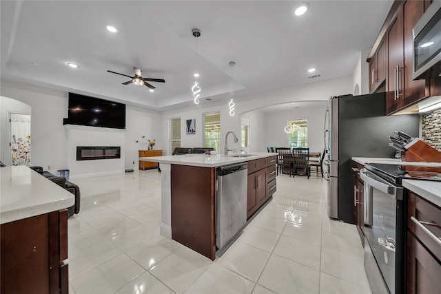 kitchen featuring an island with sink, hanging light fixtures, stainless steel appliances, and a tray ceiling