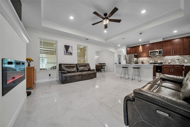 tiled living room with a tray ceiling and ceiling fan