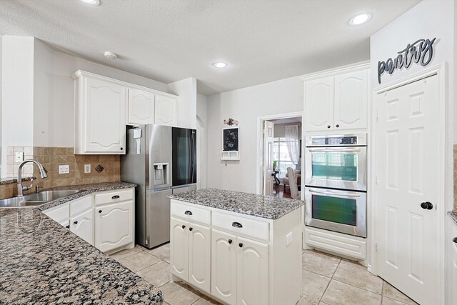 kitchen with white cabinets, a kitchen island, stone counters, sink, and stainless steel appliances