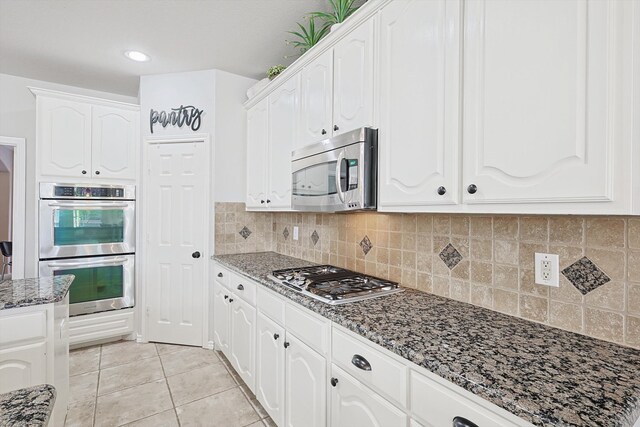 kitchen featuring light tile patterned floors, appliances with stainless steel finishes, white cabinets, and dark stone counters