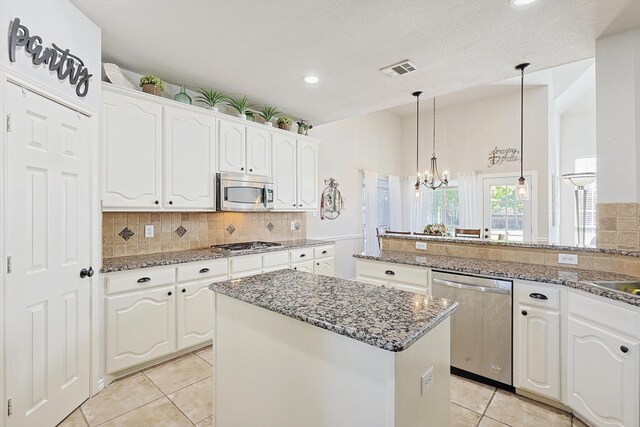 kitchen with a kitchen island, hanging light fixtures, stainless steel appliances, white cabinets, and an inviting chandelier