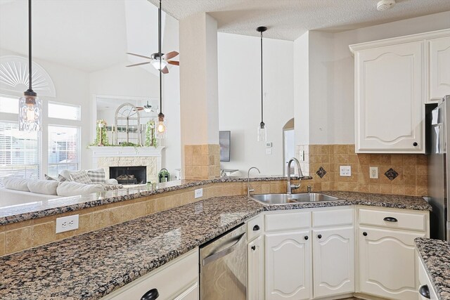 kitchen featuring a stone fireplace, hanging light fixtures, stainless steel appliances, sink, and white cabinetry