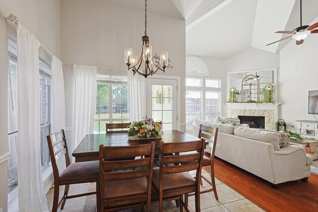 dining area featuring hardwood / wood-style flooring, high vaulted ceiling, ceiling fan with notable chandelier, and a fireplace