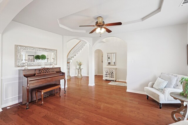 living area featuring ceiling fan, hardwood / wood-style flooring, and a raised ceiling