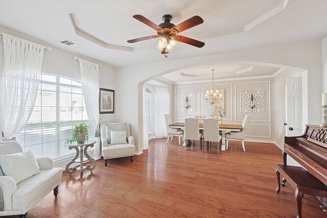 dining space with wood-type flooring, a tray ceiling, and ceiling fan with notable chandelier