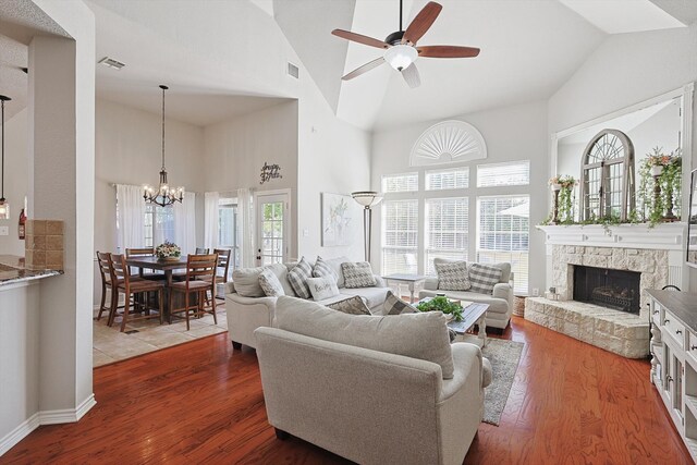 living room featuring high vaulted ceiling, a stone fireplace, wood-type flooring, and ceiling fan with notable chandelier