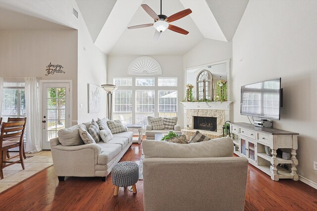 living room with a stone fireplace, wood-type flooring, high vaulted ceiling, and ceiling fan