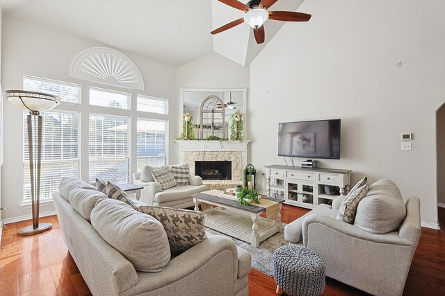 living room with a stone fireplace, dark hardwood / wood-style floors, high vaulted ceiling, and ceiling fan