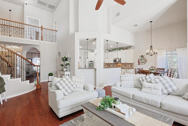 living room featuring ceiling fan with notable chandelier, a high ceiling, and dark hardwood / wood-style floors