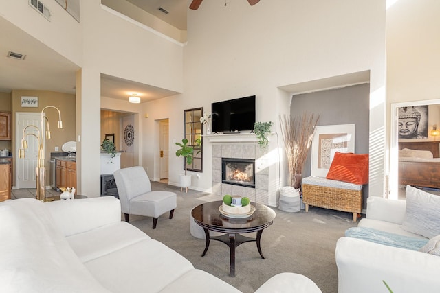 carpeted living room featuring a high ceiling, a tile fireplace, and ceiling fan