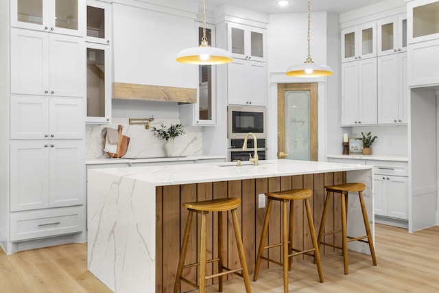 kitchen featuring white cabinets, light hardwood / wood-style floors, a center island with sink, and hanging light fixtures