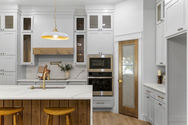 kitchen featuring light stone counters, appliances with stainless steel finishes, a kitchen bar, sink, and decorative light fixtures