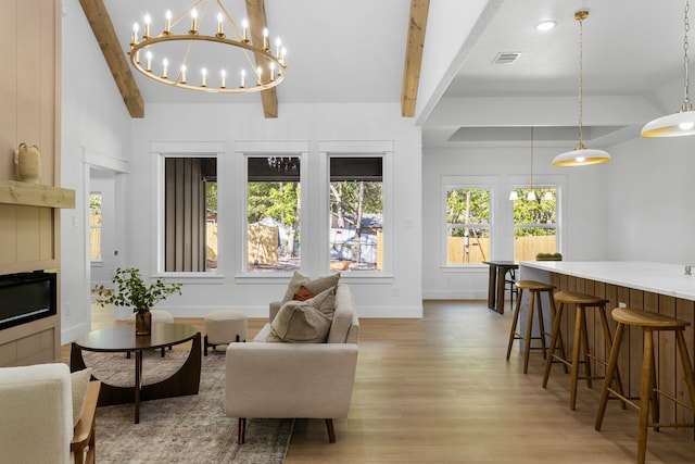 living room with lofted ceiling with beams, a chandelier, and light wood-type flooring