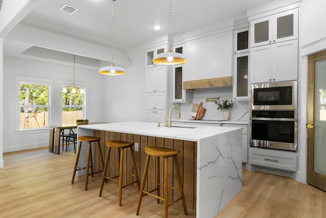 kitchen featuring white cabinets, hanging light fixtures, appliances with stainless steel finishes, a kitchen island with sink, and sink