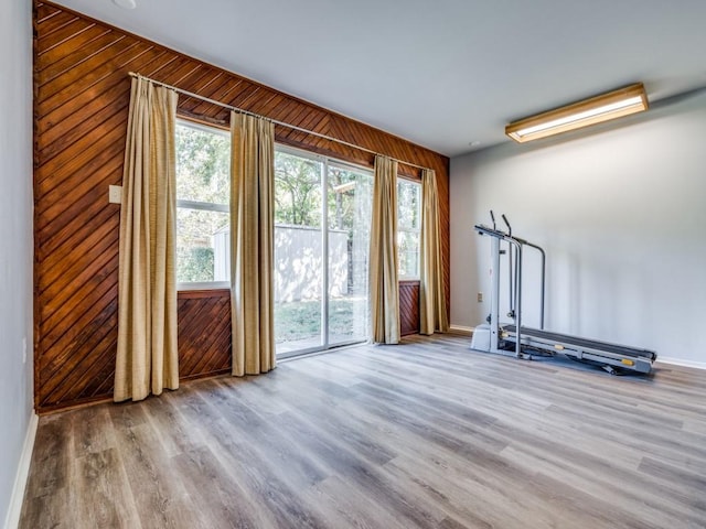 exercise area with light wood-type flooring and wooden walls