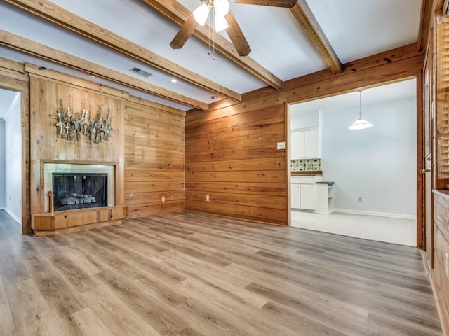 unfurnished living room featuring beamed ceiling, ceiling fan, wood walls, and light hardwood / wood-style flooring