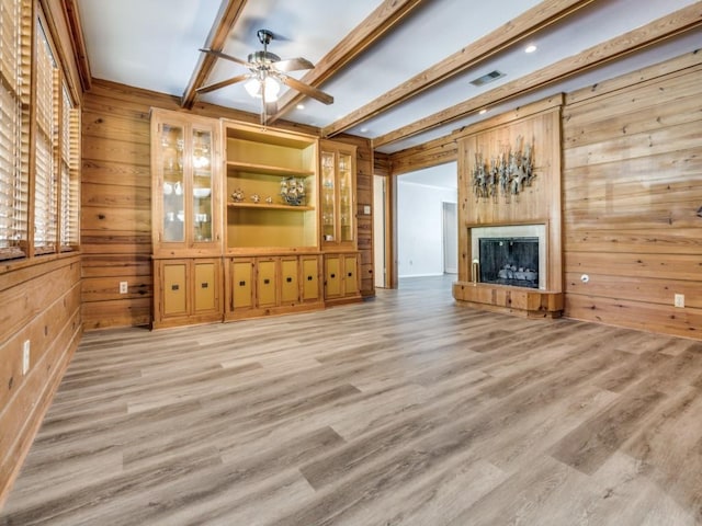 unfurnished living room featuring beam ceiling, wooden walls, and light hardwood / wood-style flooring