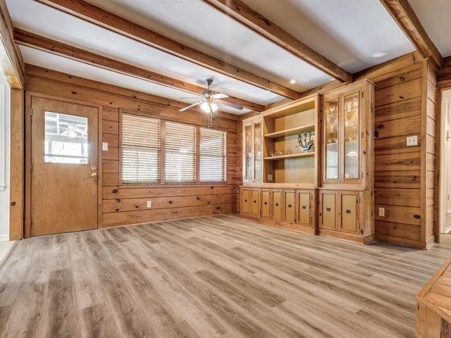 interior space with ceiling fan, wood walls, beam ceiling, and light hardwood / wood-style flooring