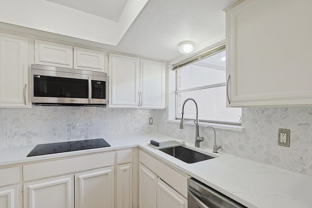 kitchen featuring tasteful backsplash, white cabinetry, sink, stainless steel appliances, and light stone countertops