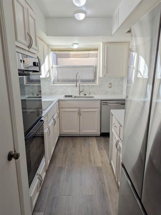 kitchen with tasteful backsplash, sink, white cabinets, stainless steel appliances, and light hardwood / wood-style flooring