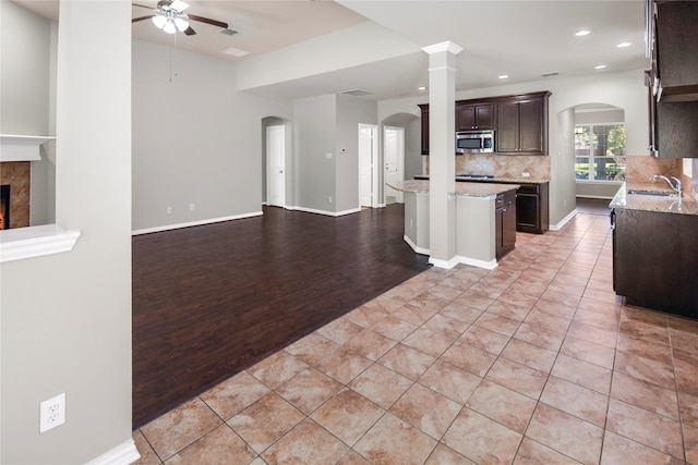 kitchen with light stone countertops, light hardwood / wood-style flooring, ornate columns, dark brown cabinetry, and a center island