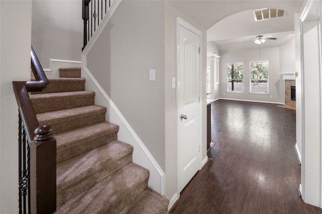 stairs featuring hardwood / wood-style floors, a tiled fireplace, and ceiling fan