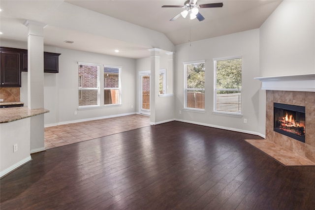 unfurnished living room with lofted ceiling, ceiling fan, a tile fireplace, dark wood-type flooring, and ornate columns