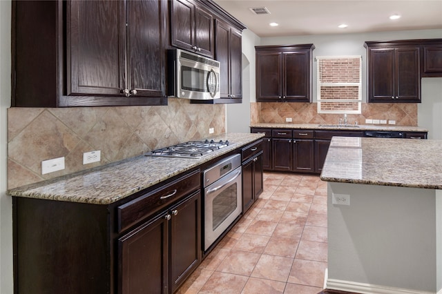 kitchen with tasteful backsplash, appliances with stainless steel finishes, light stone countertops, dark brown cabinetry, and sink