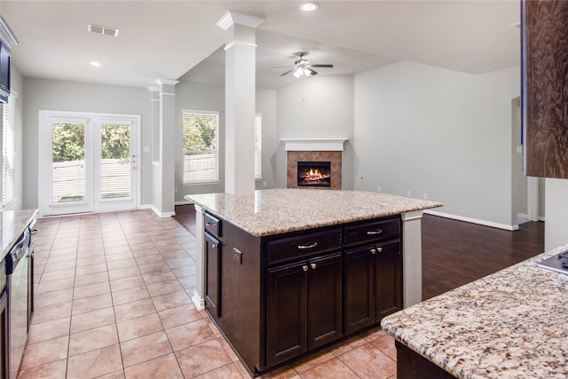 kitchen with light stone countertops, a kitchen island, ornate columns, ceiling fan, and light tile patterned floors