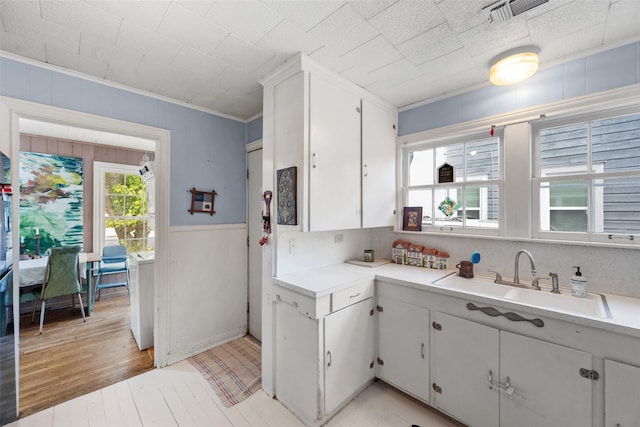 kitchen with light hardwood / wood-style floors, crown molding, white cabinetry, and sink