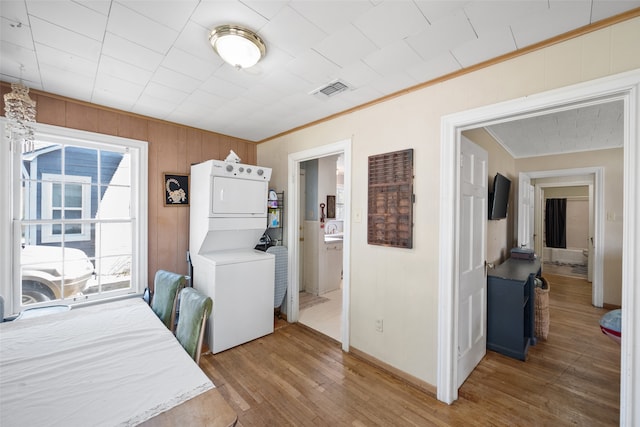 laundry area featuring hardwood / wood-style floors, stacked washer and clothes dryer, crown molding, and wooden walls