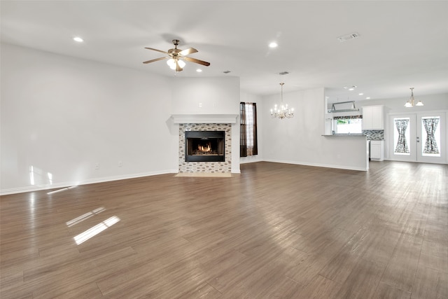 unfurnished living room with a fireplace, dark wood-type flooring, ceiling fan with notable chandelier, and french doors