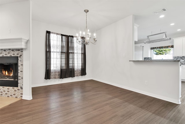 unfurnished dining area featuring dark hardwood / wood-style flooring, a brick fireplace, and a notable chandelier