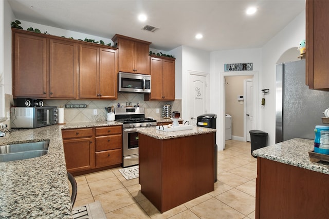 kitchen with a kitchen island, sink, light tile patterned floors, appliances with stainless steel finishes, and light stone counters