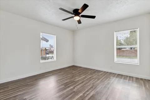 empty room with a healthy amount of sunlight, dark wood-type flooring, and ceiling fan