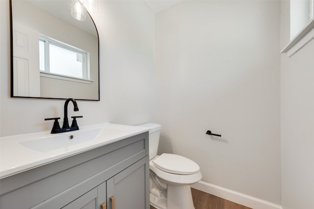 bathroom with wood finished floors, vanity, toilet, and baseboards