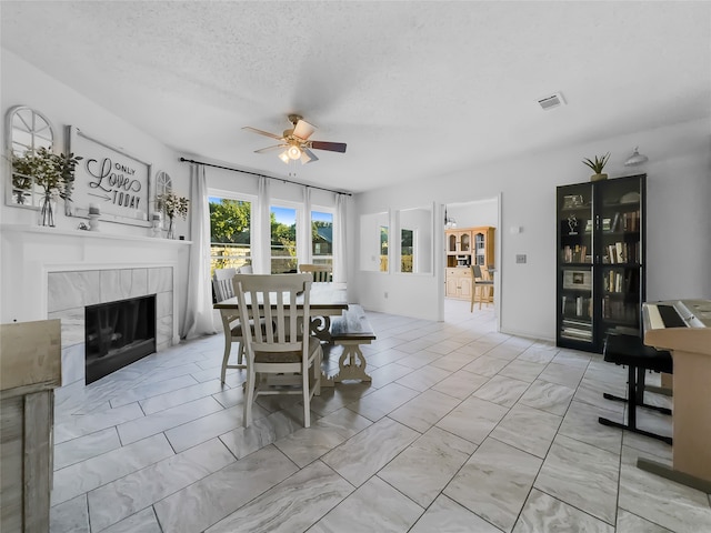 dining area featuring a tiled fireplace, ceiling fan, and a textured ceiling