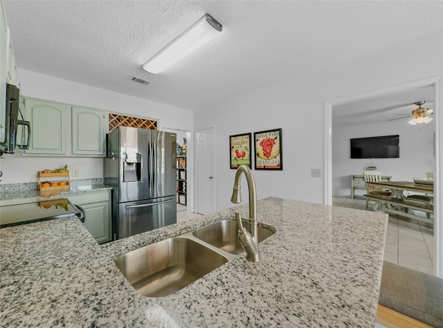 kitchen with sink, green cabinetry, range, a textured ceiling, and stainless steel fridge