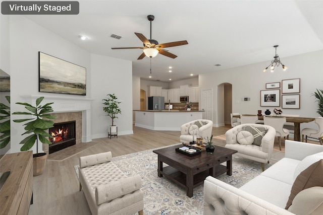 living room with ceiling fan with notable chandelier, light wood-type flooring, and a tiled fireplace