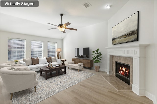 living room with light hardwood / wood-style flooring, ceiling fan, lofted ceiling, and a tiled fireplace