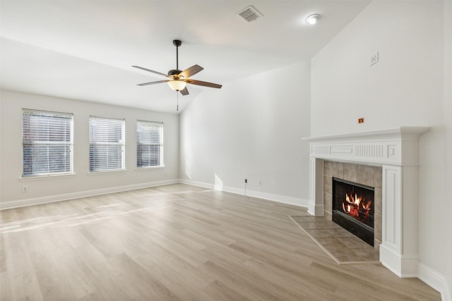 unfurnished living room featuring a tiled fireplace, ceiling fan, lofted ceiling, and light wood-type flooring