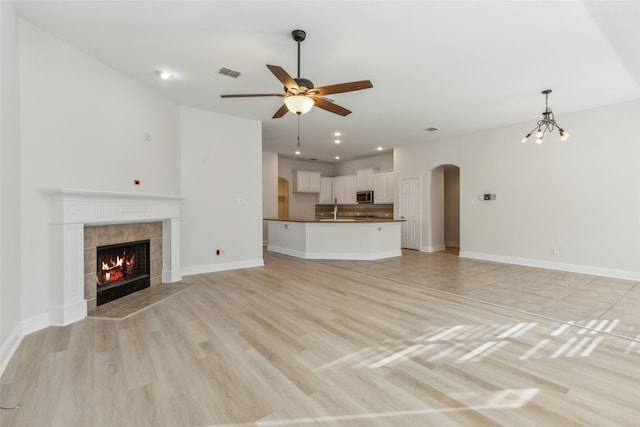 unfurnished living room featuring a fireplace, light wood-type flooring, ceiling fan with notable chandelier, and sink