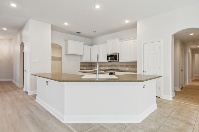 kitchen with white cabinets, decorative backsplash, dark stone countertops, and an island with sink