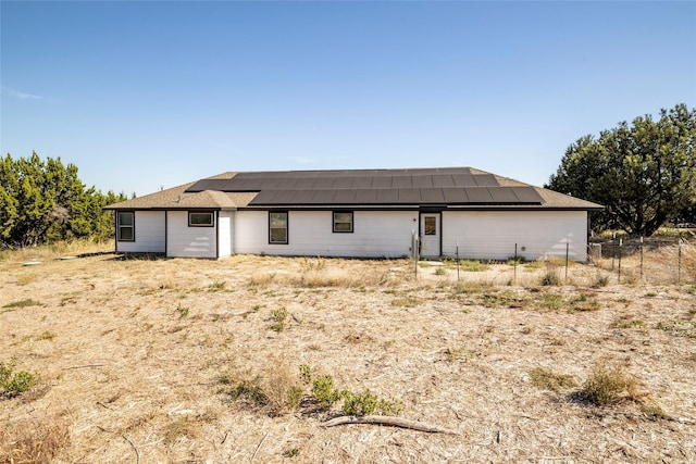 rear view of house featuring fence and solar panels