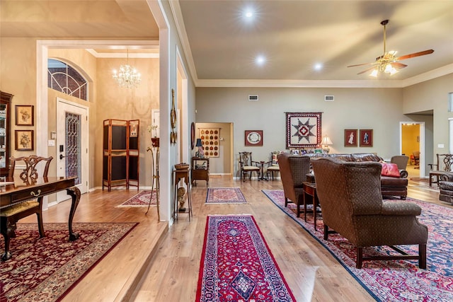 living room featuring crown molding, a towering ceiling, light hardwood / wood-style floors, and ceiling fan with notable chandelier