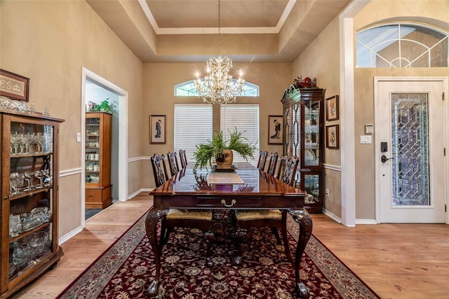 dining room with a notable chandelier, a raised ceiling, light wood-type flooring, and a towering ceiling