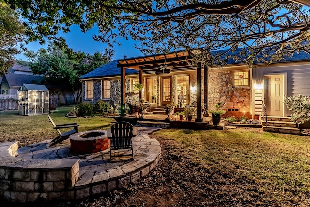 back of house featuring a yard, an outdoor fire pit, a shed, and ceiling fan