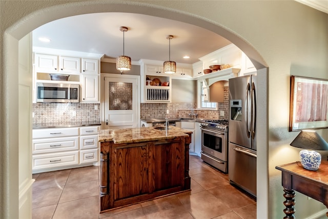 kitchen featuring a center island, white cabinetry, stainless steel appliances, decorative light fixtures, and light stone counters